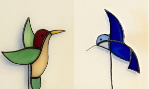 Two stained glass hummingbirds. On the left is a yellow, green, and red figure. On the right is a navy blue bird with a light blue head. Both come with planters